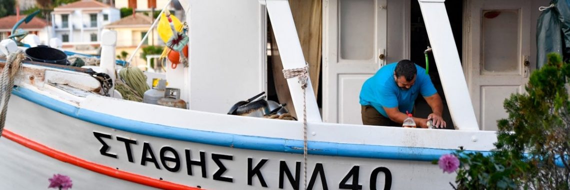 Authentic Greek fisherman working on a traditional white fishing boat in a picturesque Mediterranean harbor.